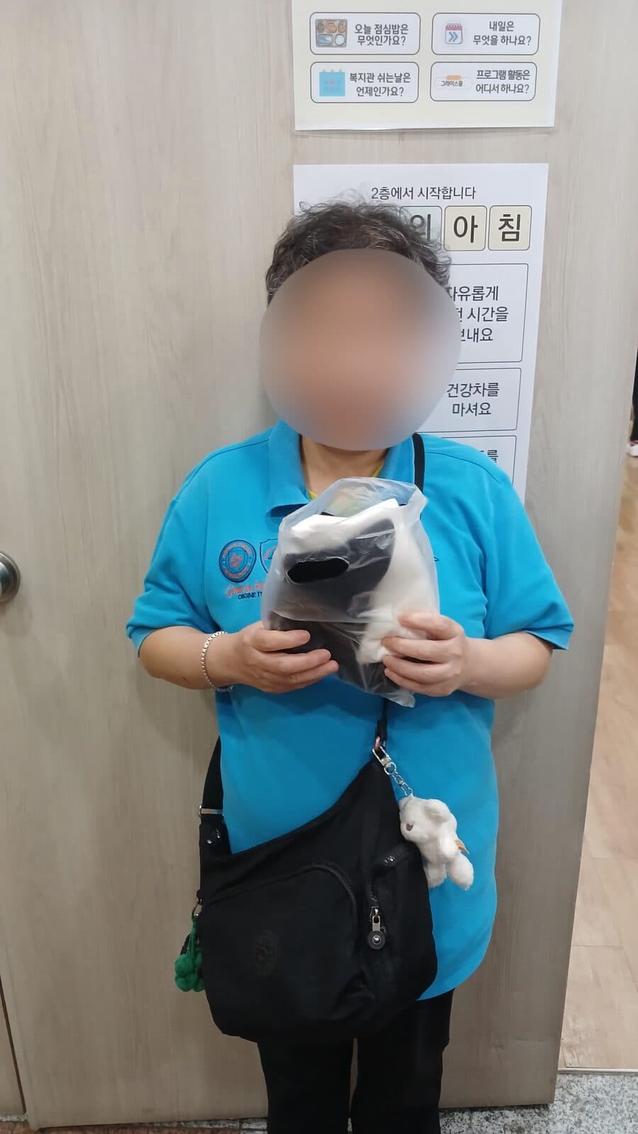 복지관 실내에서 가방을 멘 사람이 양말이 담긴 봉투를 두 손으로 들고 있다.